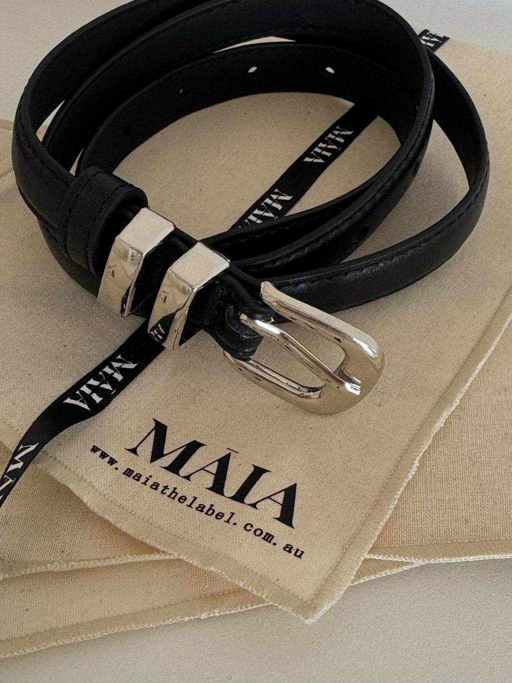 Black leather Celia Belt with silver chrome buckle, 100cm length, resting on Maia Label branded cloth pouch.