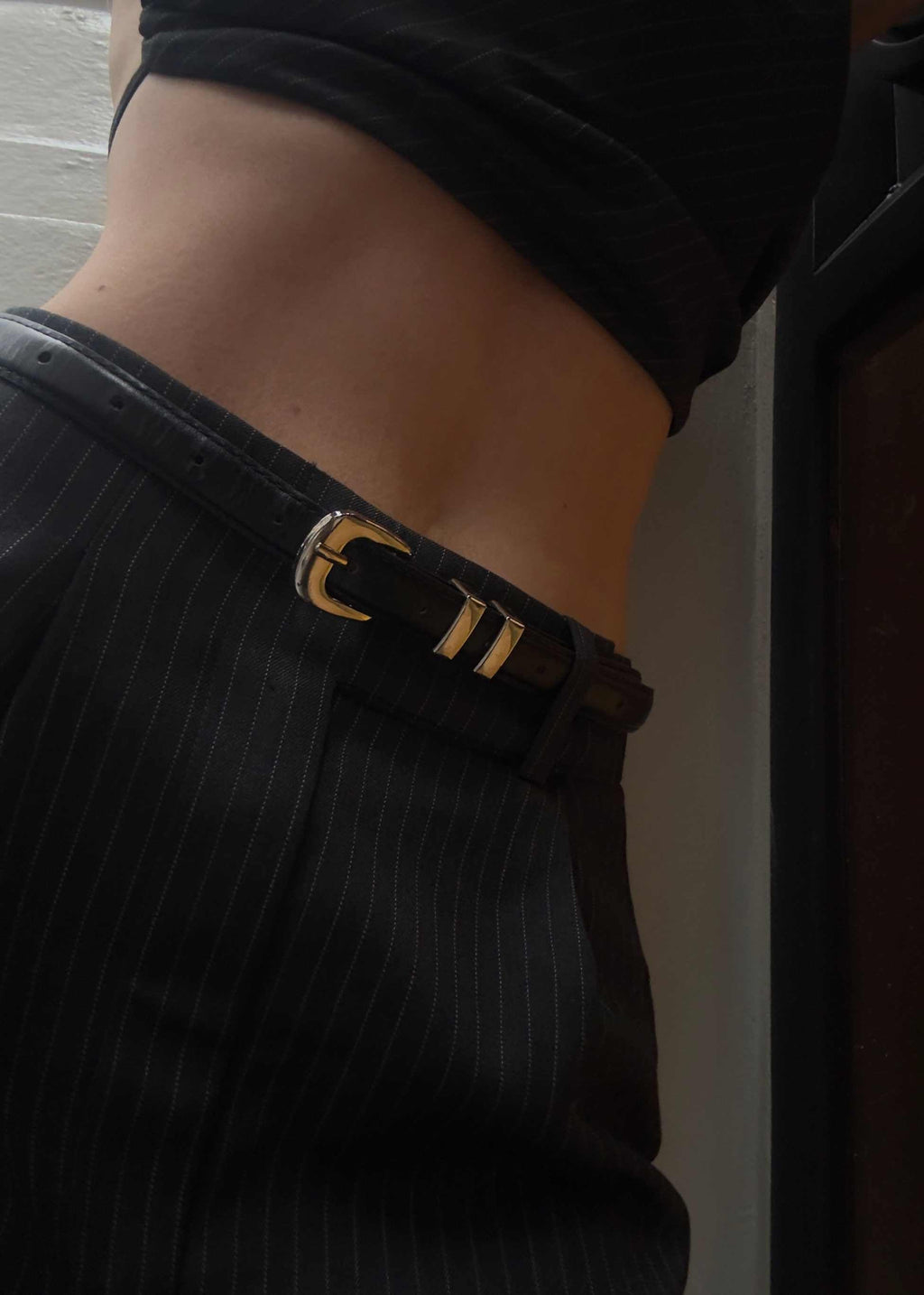 Black leather Celia Belt with silver chrome buckle worn on pinstripe pants