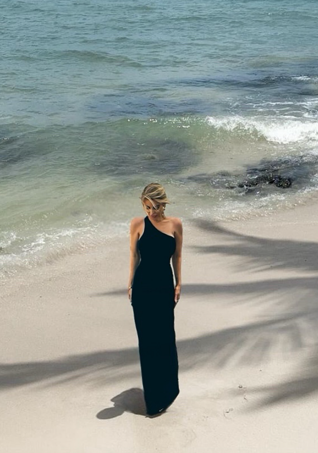 Woman in a black dress standing on a sandy beach with ocean waves in the background