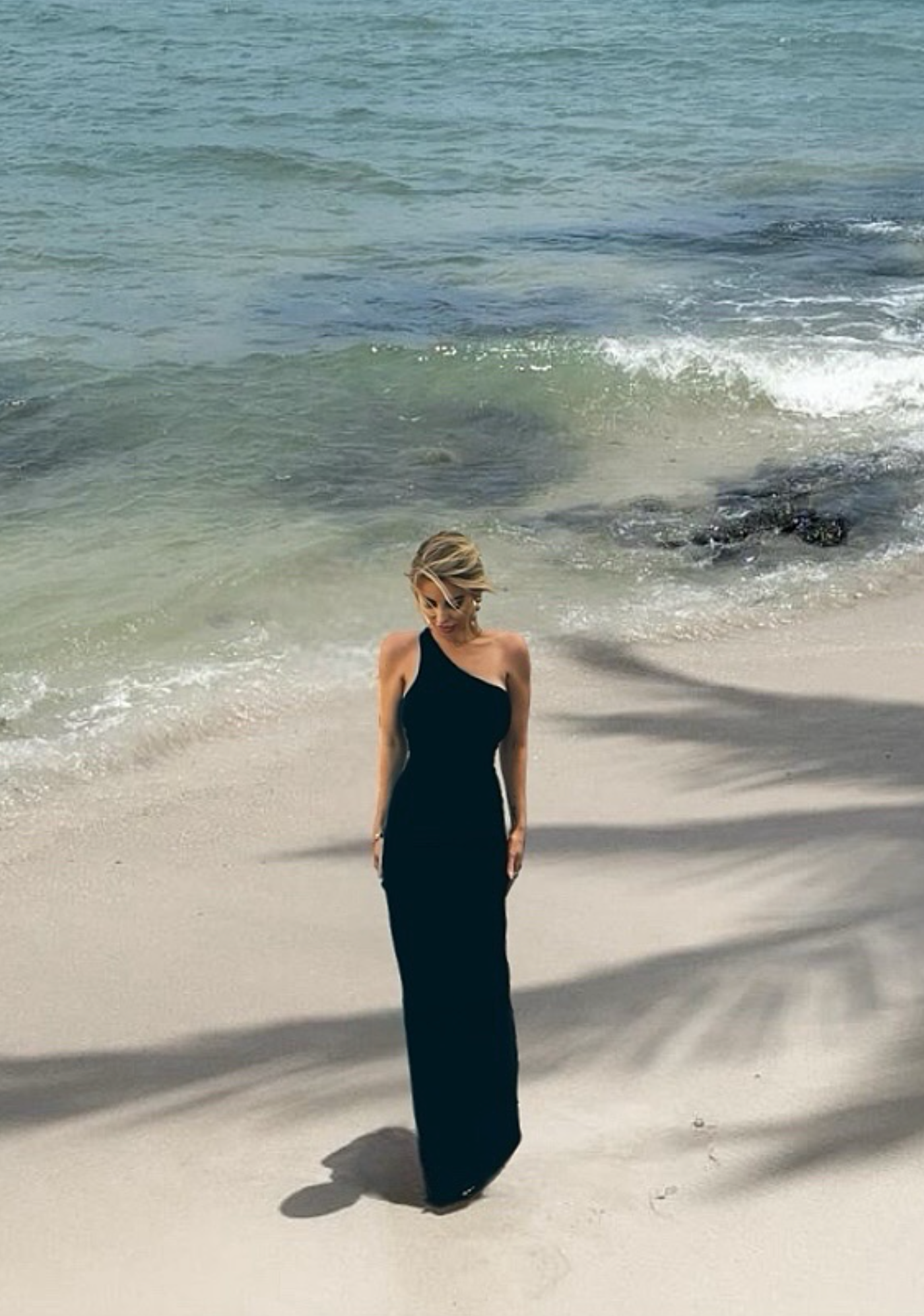 Woman in a black dress standing on a sandy beach with ocean waves in the background